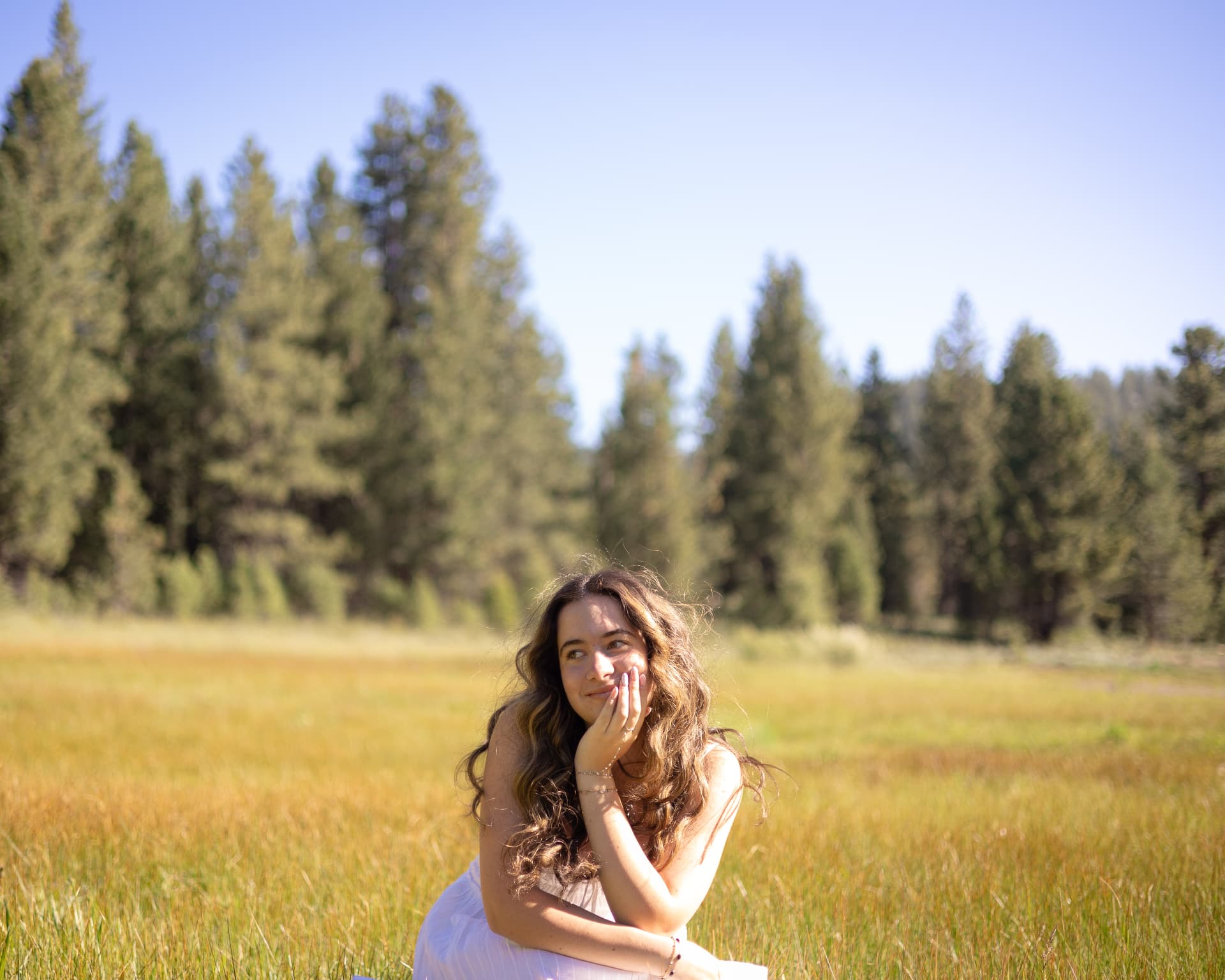 Senior portrait of a young woman resting her chin on her hand in a sunlit mountain meadow