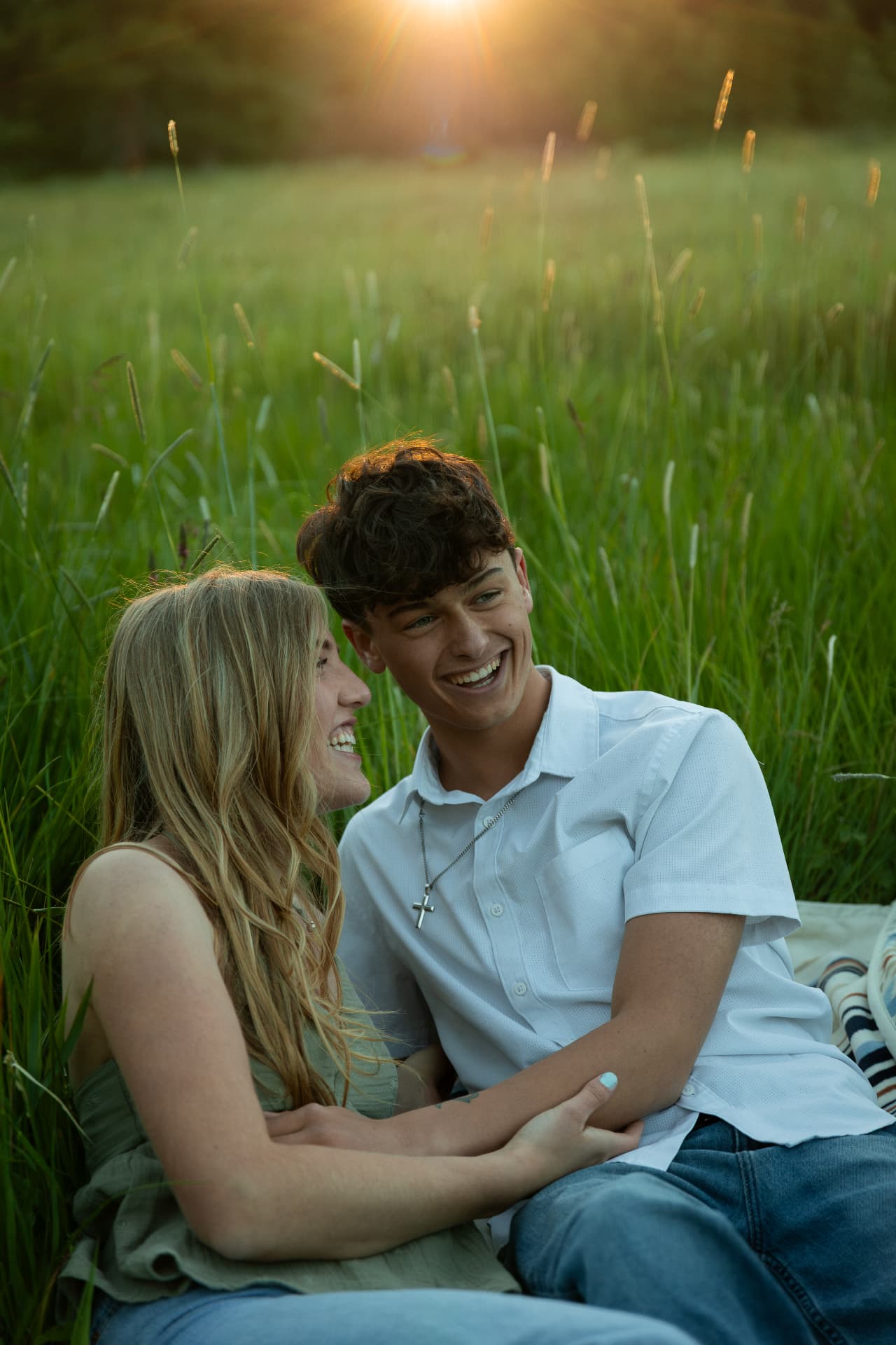 Couple laughing together in tall summer grass at sunset